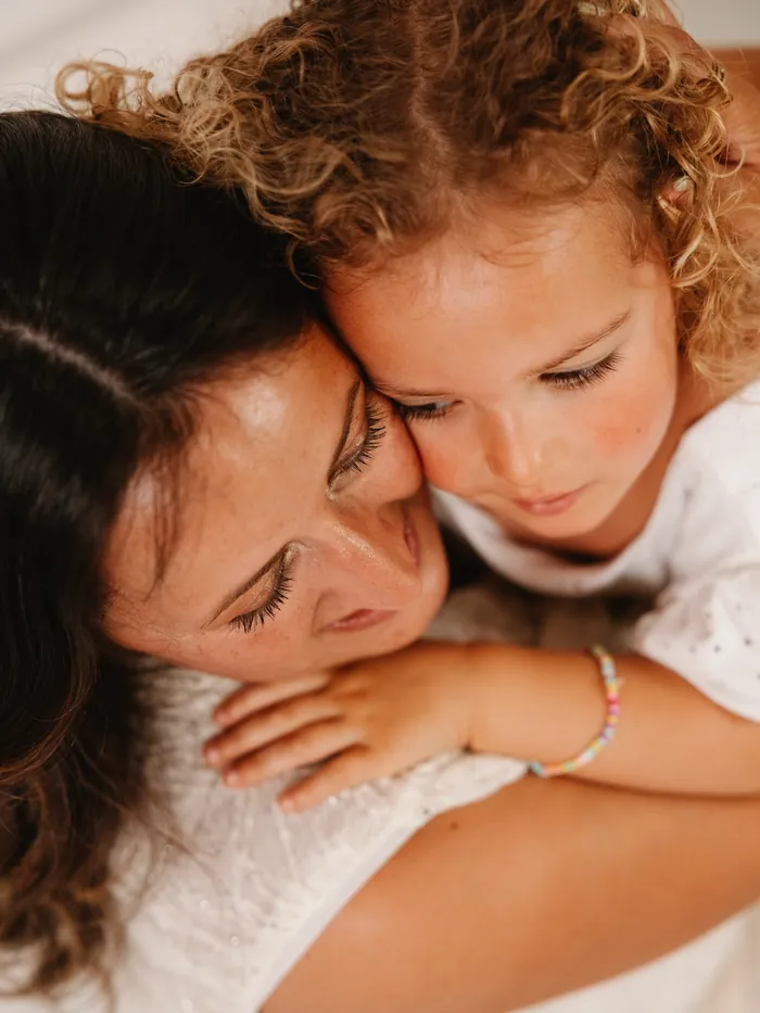 Uma menina de caracóis abraçada à mãe, cara com cara.