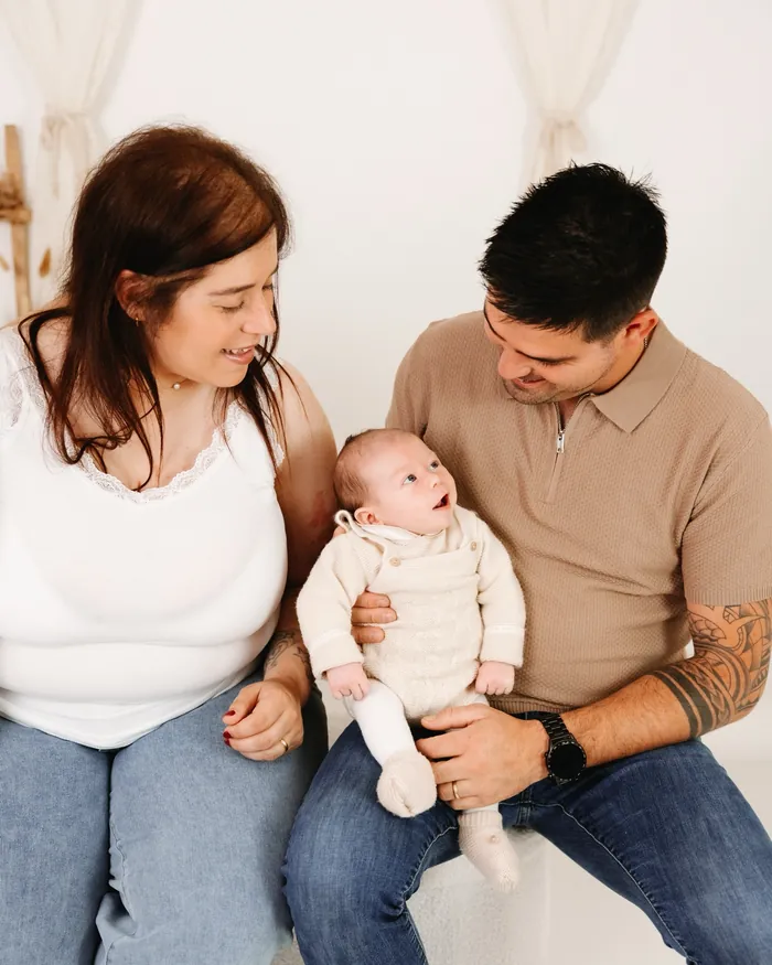 Pai e mãe sentados num banco, no estúdio, com o bebé de um mês ao colo.