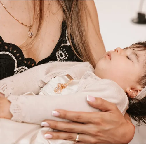 Bebé a dormir ao colo da mãe, vestido para o batizado.