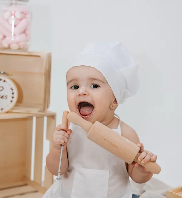 Bebé de chapéu de cozinheiro e avental, com um rolo da massa, num mesversário com tema de padeiro.