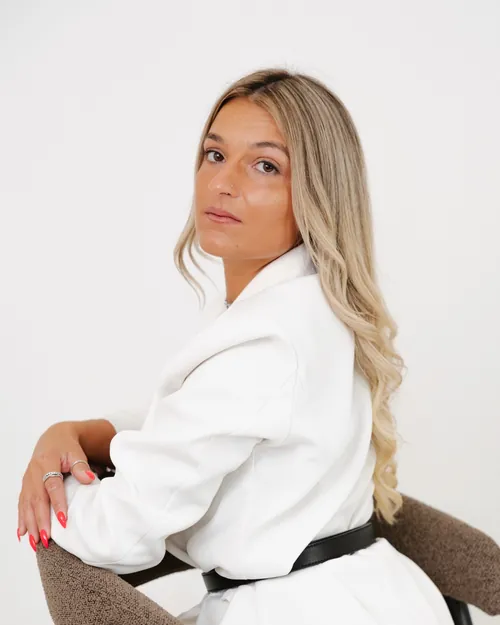 Retrato de uma mulher de blazer branco, sentada no estúdio.
